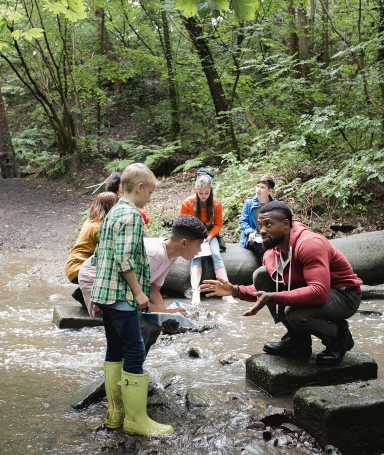 Group of school children on a field trip. They are standing in a river. Credit iStore