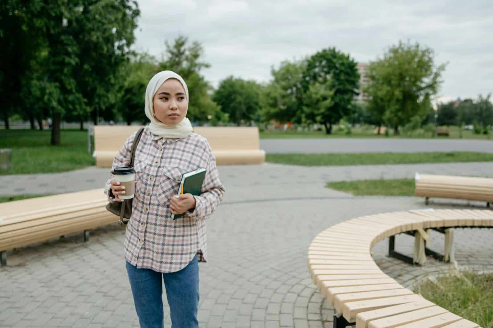 Young woman in head scarf walking near seating area in park. Credit Pixabay